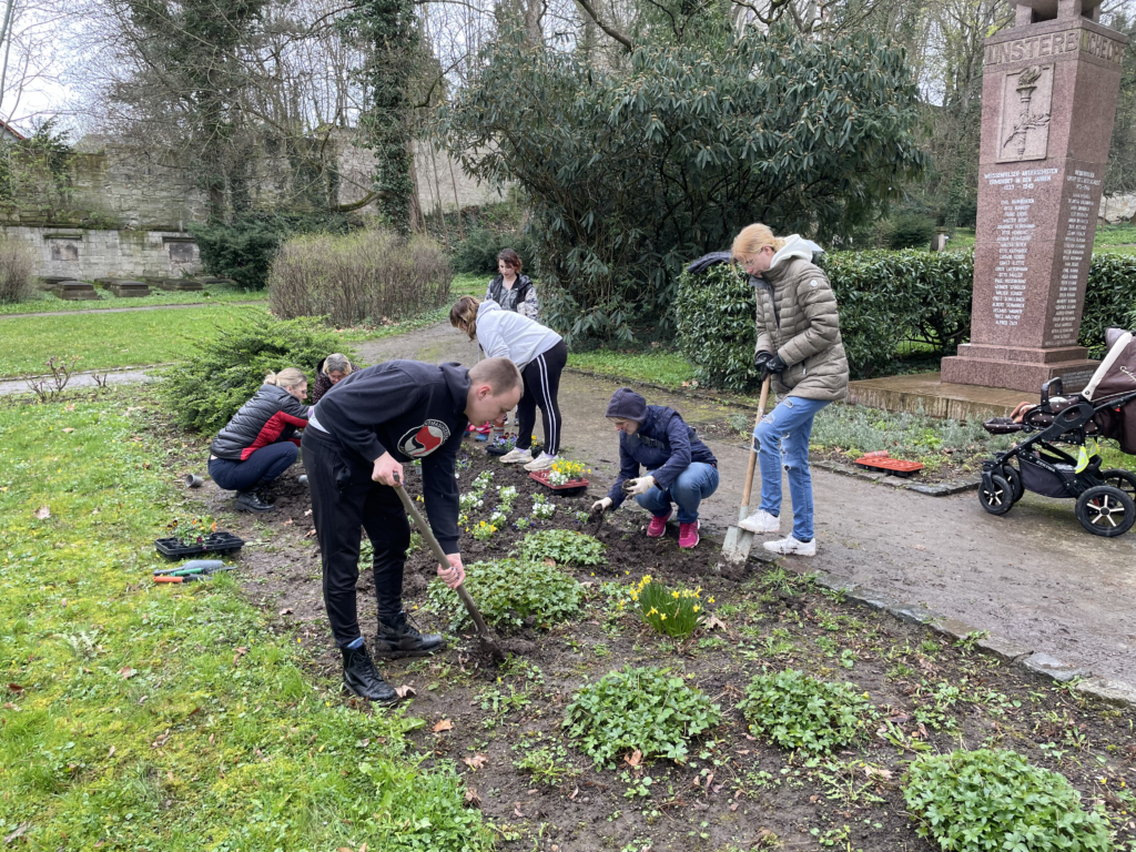 Eine Gruppe aus Menschen der Initiative pflanzt Blumen im Park. Zu sehen sind Kinder und Erwachsene mit Spaten am Pflanzen und Vorbereiten.