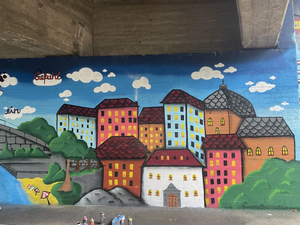 Zu sehen ist ein Graffiti mit einer fiktiven Stadtlandschaft, die Schüler:innen gestaltet haben.